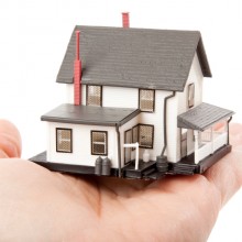 L'image représente une petite maison dans la paume d'une main ouverte, symbole du rachat credit immobilier sur notre site.