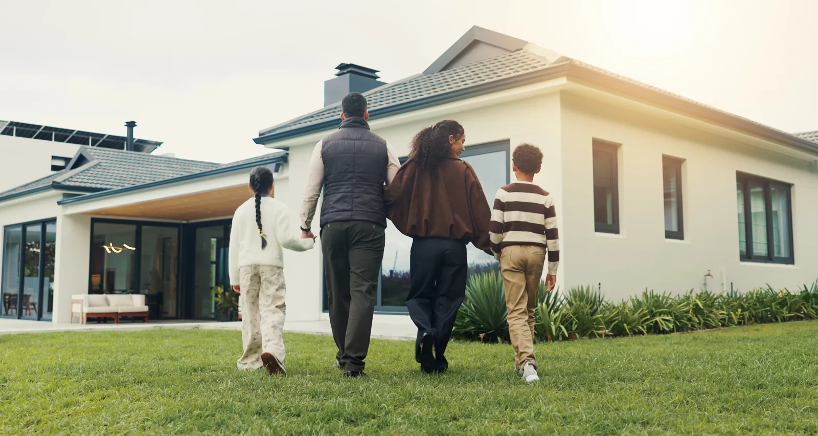 Une famille marche main dans la main devant sa maison, illustration d'un rachat de prêt immobilier